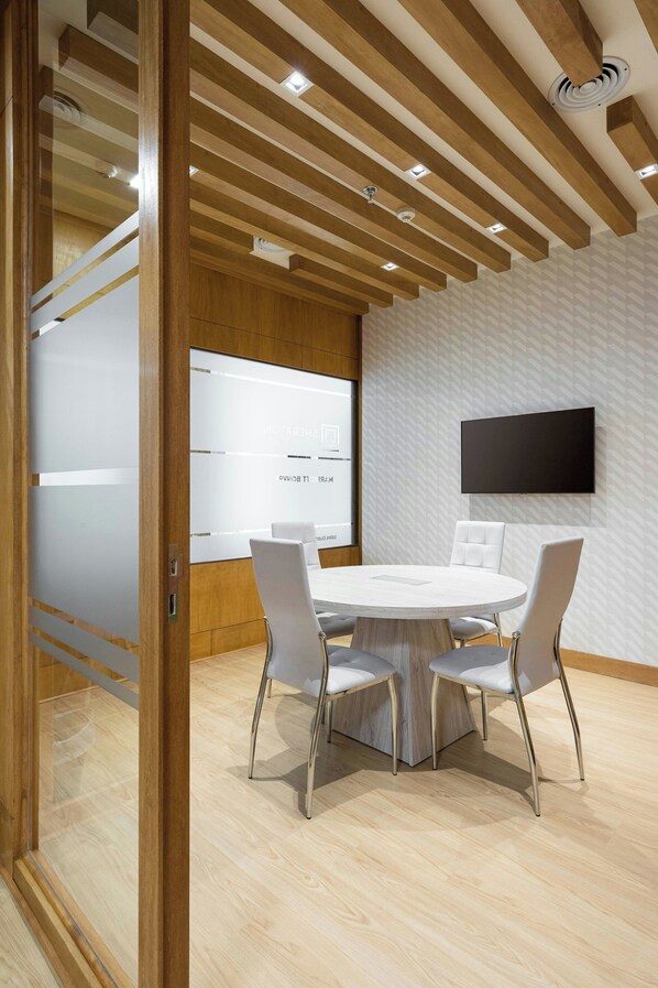 A modern meeting room with a round table, white chairs, wooden ceiling beams, and a mounted TV. - Sheraton Buenos Aires Hotel and Convention Center (Buenos Aires)