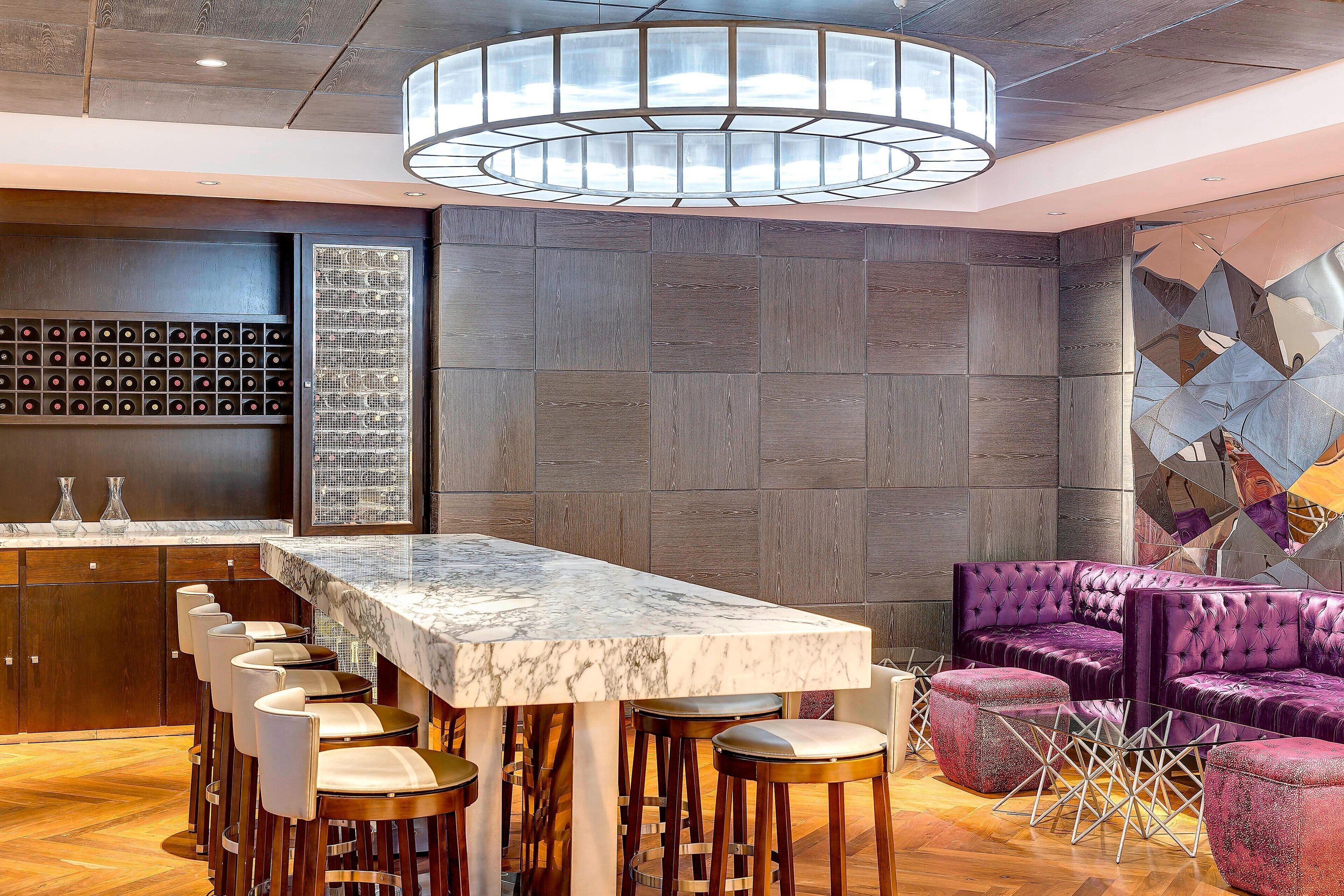 Eine Bar mit einer Marmorplatte, Barhocker und einer Sitzecke mit einer gepolsterten Couch und Hocker.