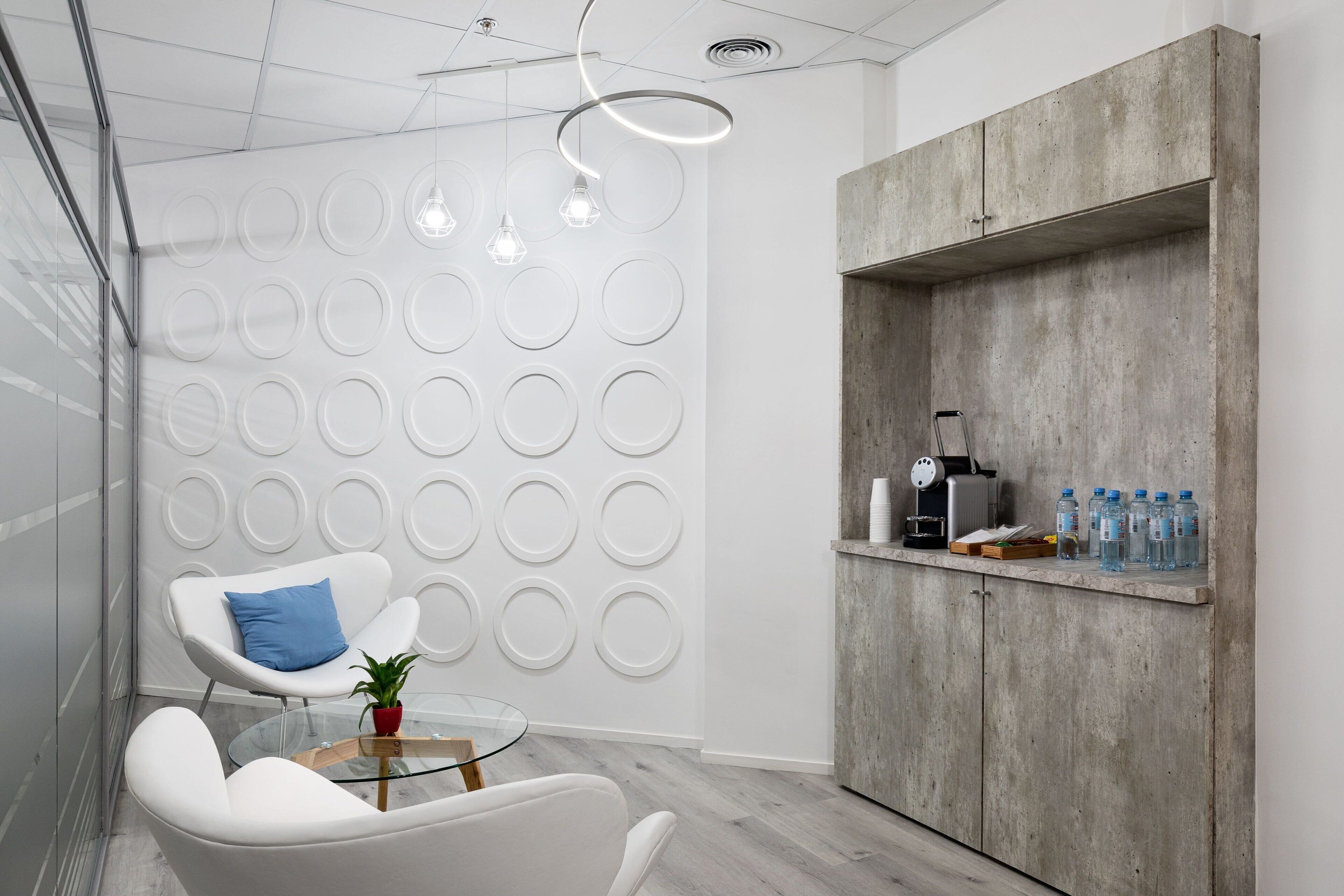 A modern office space with a white chair, a glass table, and a concrete cabinet with water bottles.