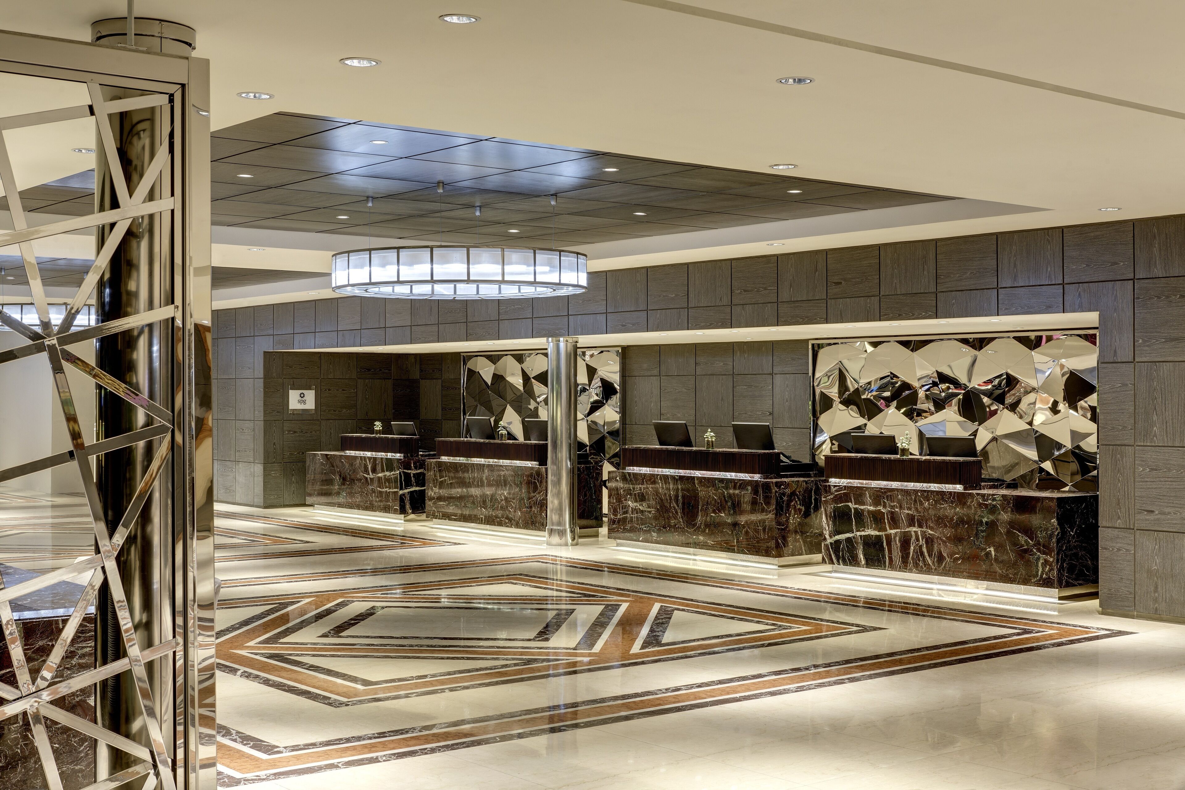 A modern lobby with marble reception desks, geometric wall art, and a patterned floor.