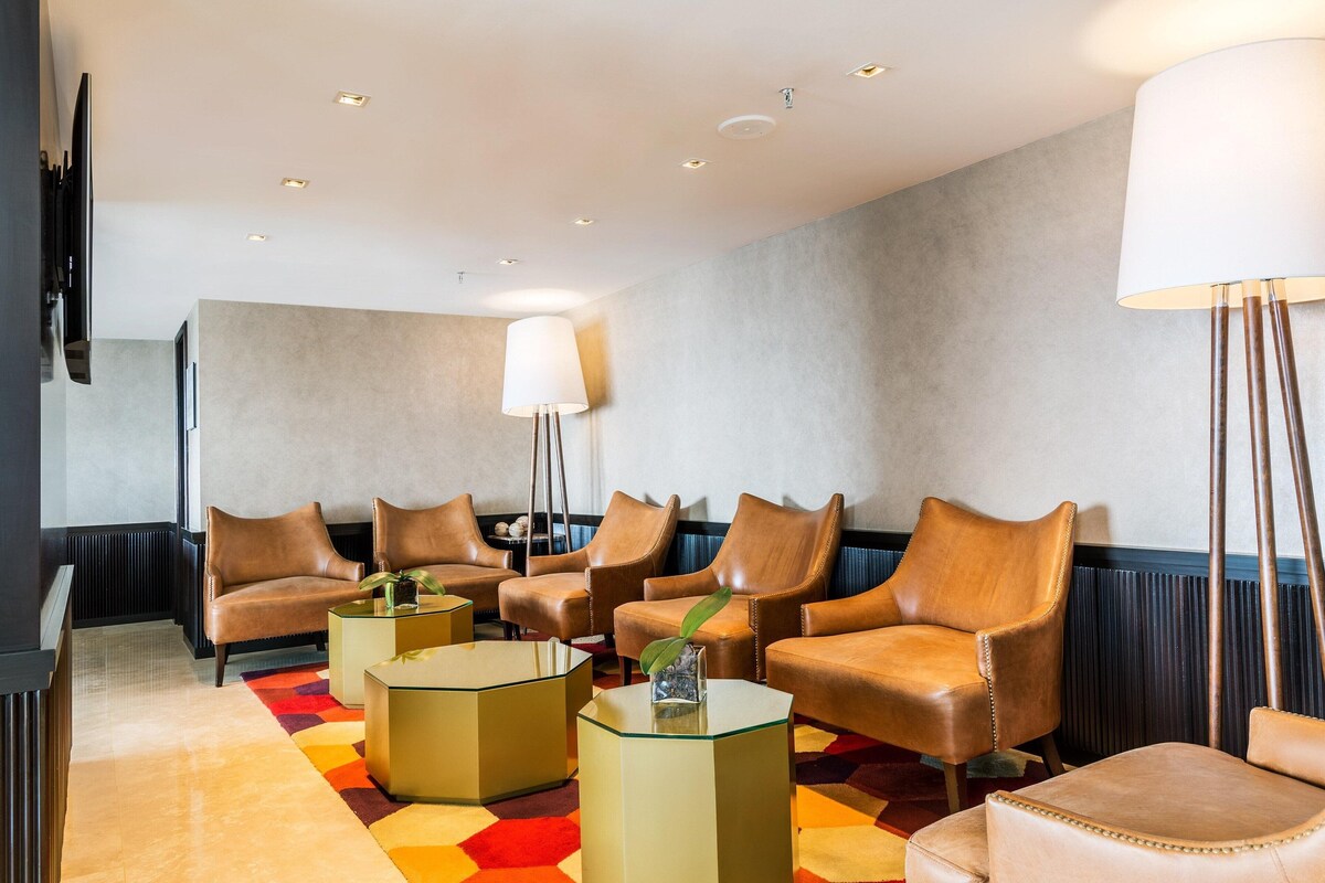 A modern lounge with leather chairs, glass tables, and a large floor lamp.