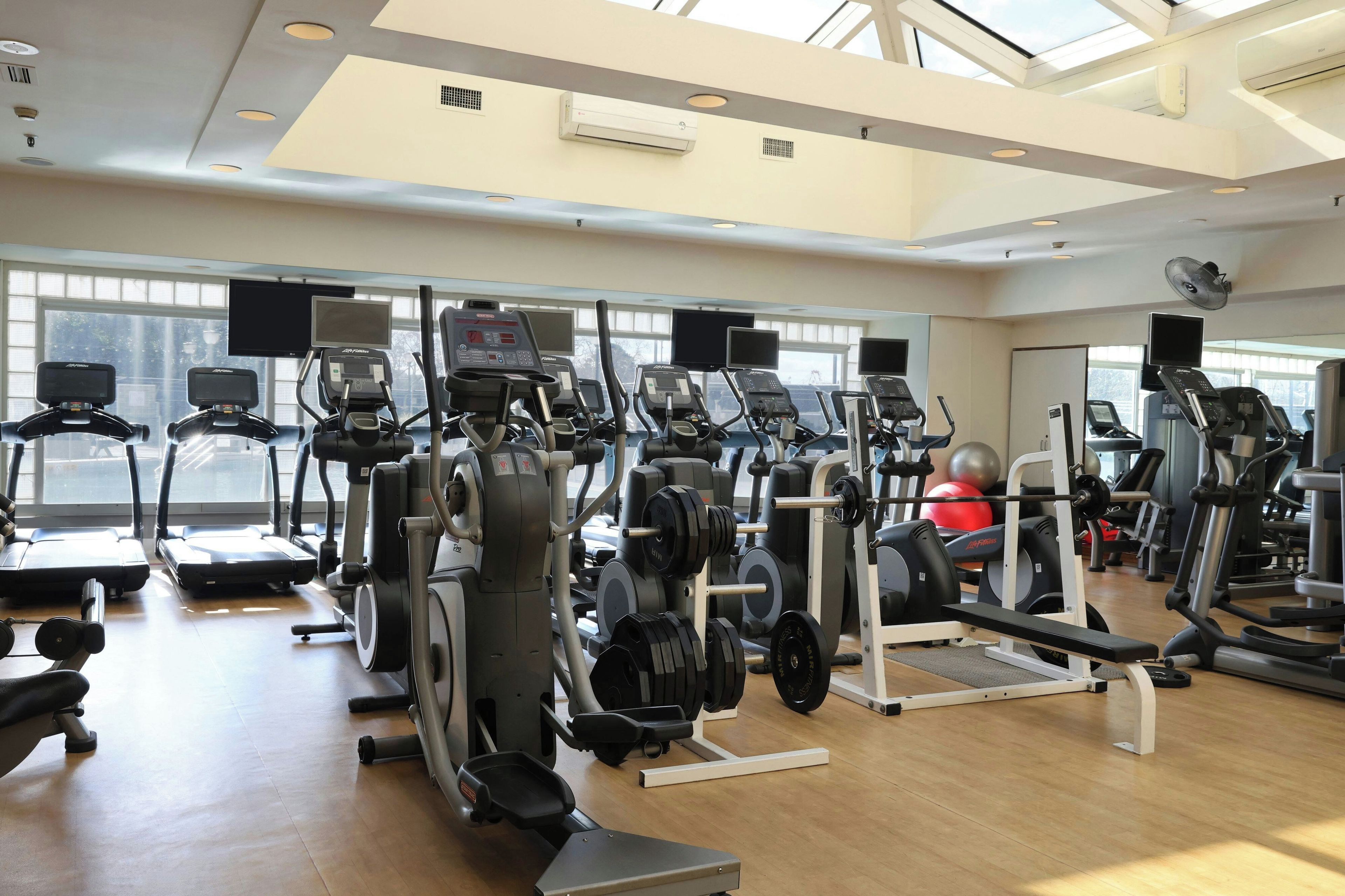 A gym with multiple treadmills, weight machines, and a large window providing natural light.