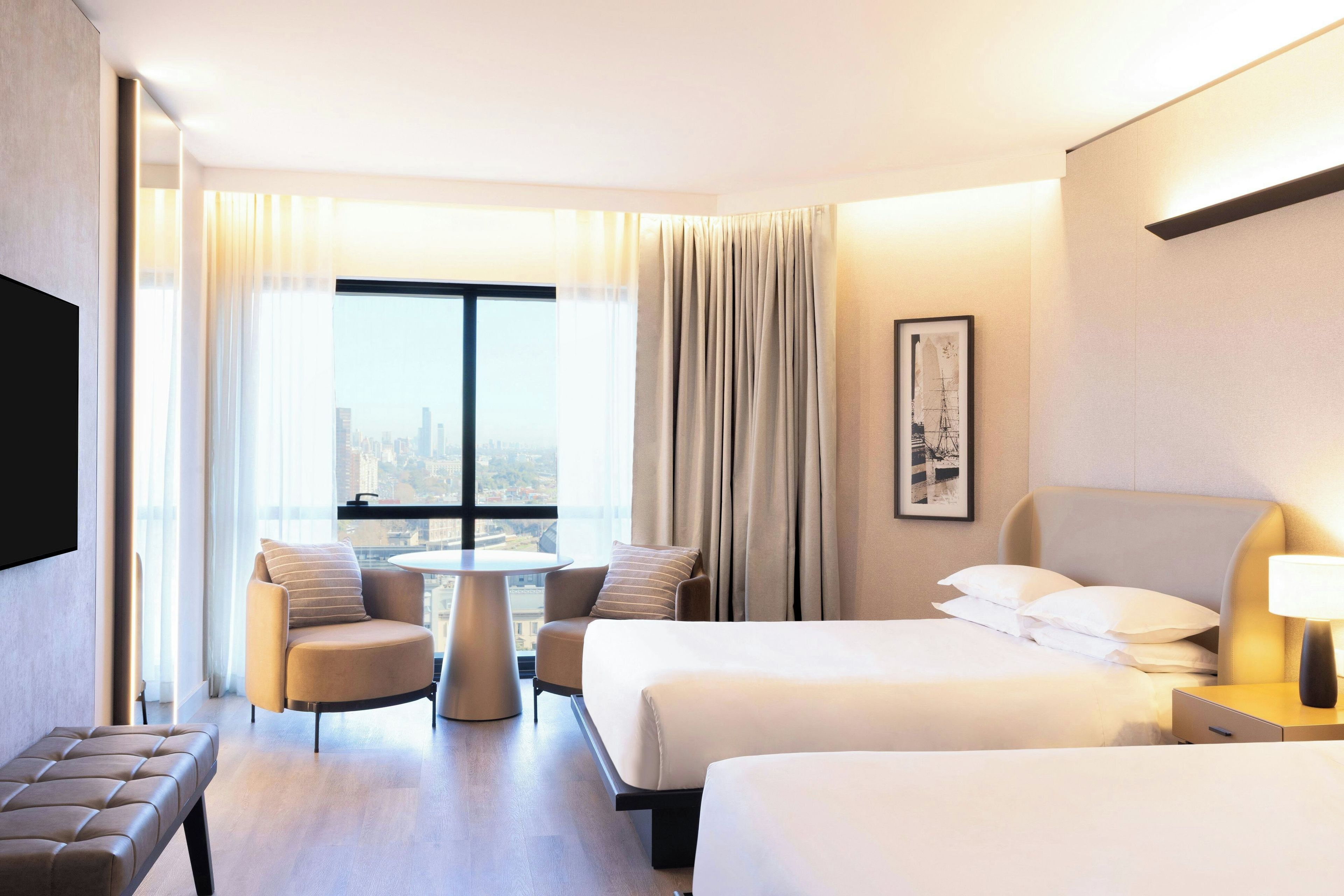 Quarto de hotel com duas camas, um sofá, uma mesa pequena e uma televisão.