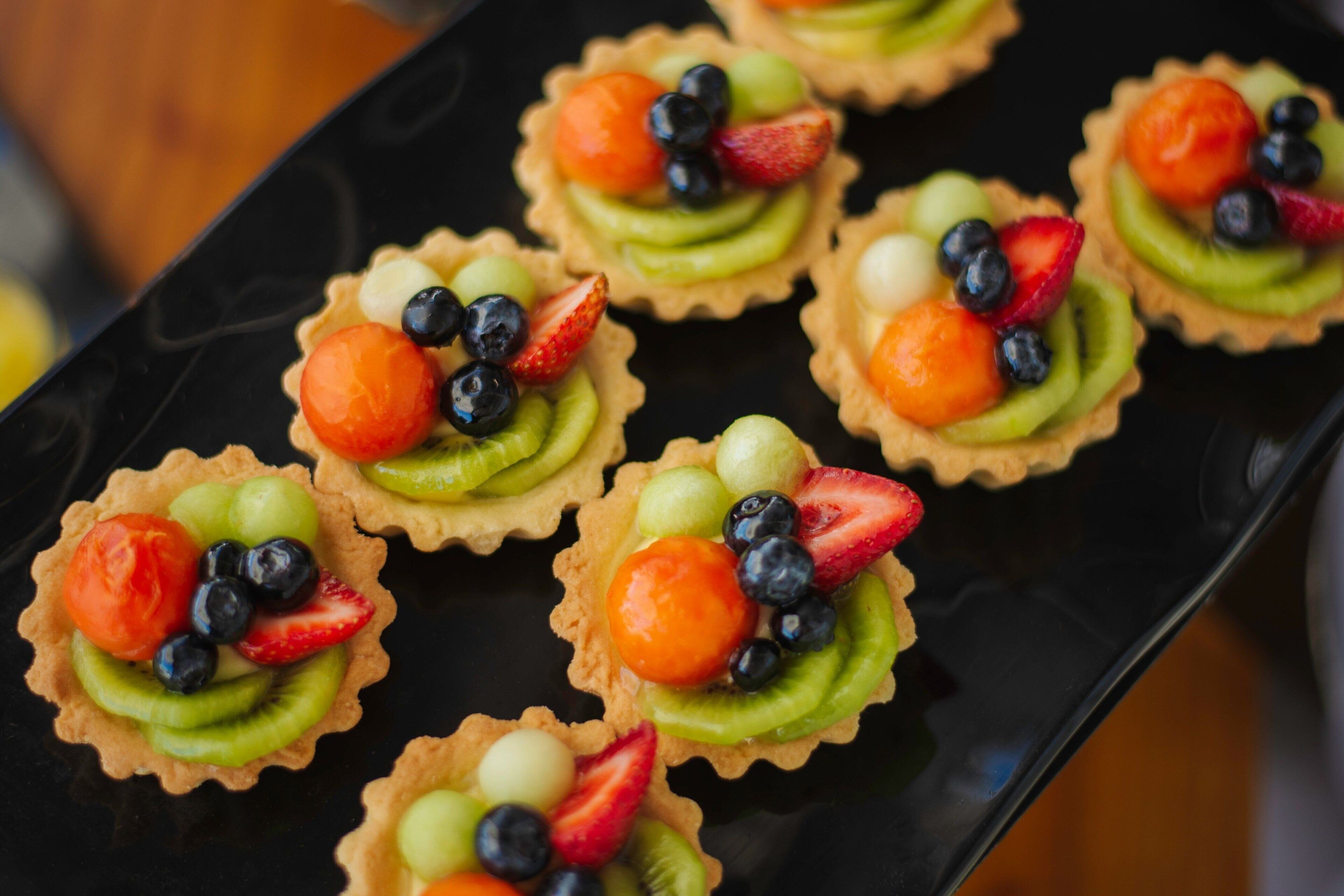 Een schaal met fruitgebakjes, met verschillende soorten fruit zoals aardbeien, blauwe bessen en kiwi.