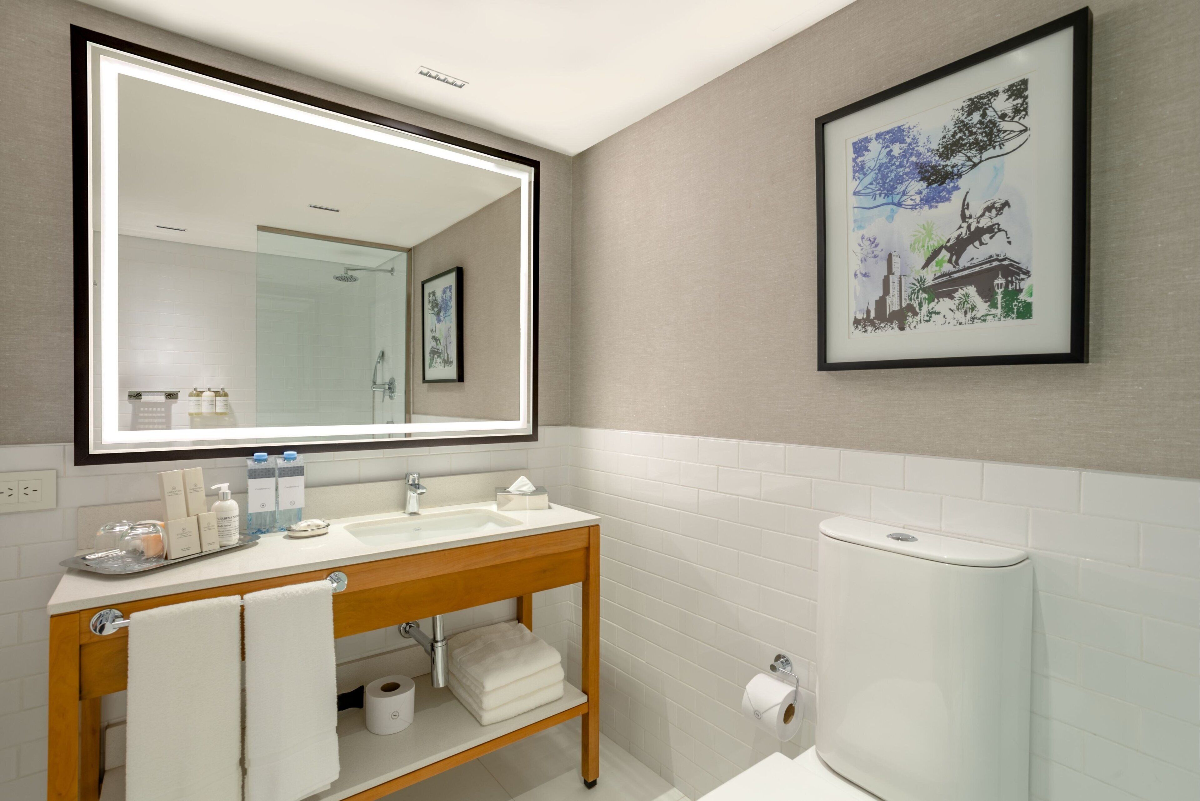 A modern bathroom with a large mirror, white tiles, a wooden vanity, and a toilet paper holder.