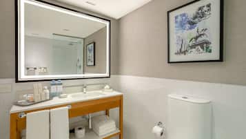 A modern bathroom with a large mirror, white tiles, a wooden vanity, and a toilet paper holder.
