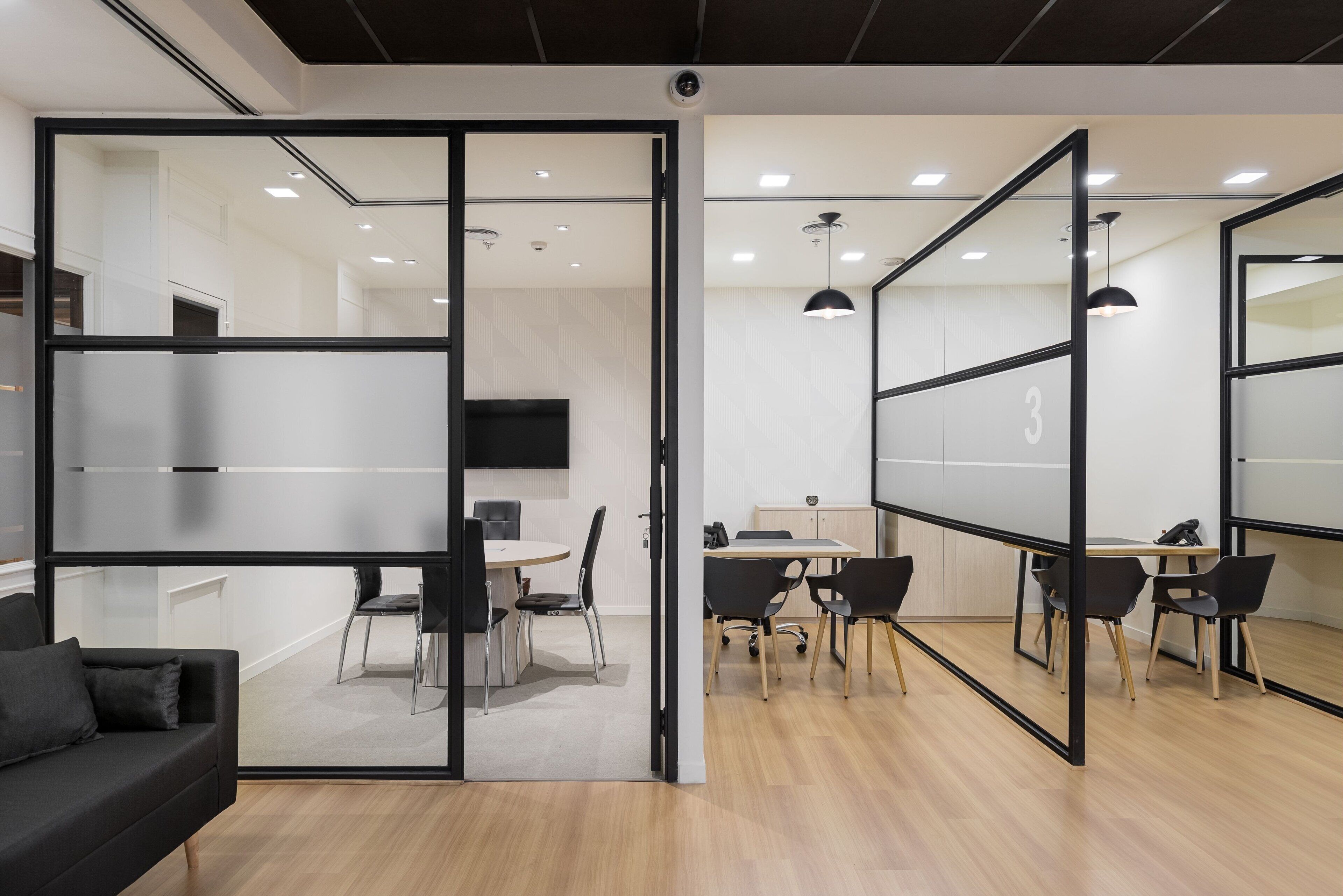 An office space with glass partitions, a black sofa, and a meeting table with chairs.
