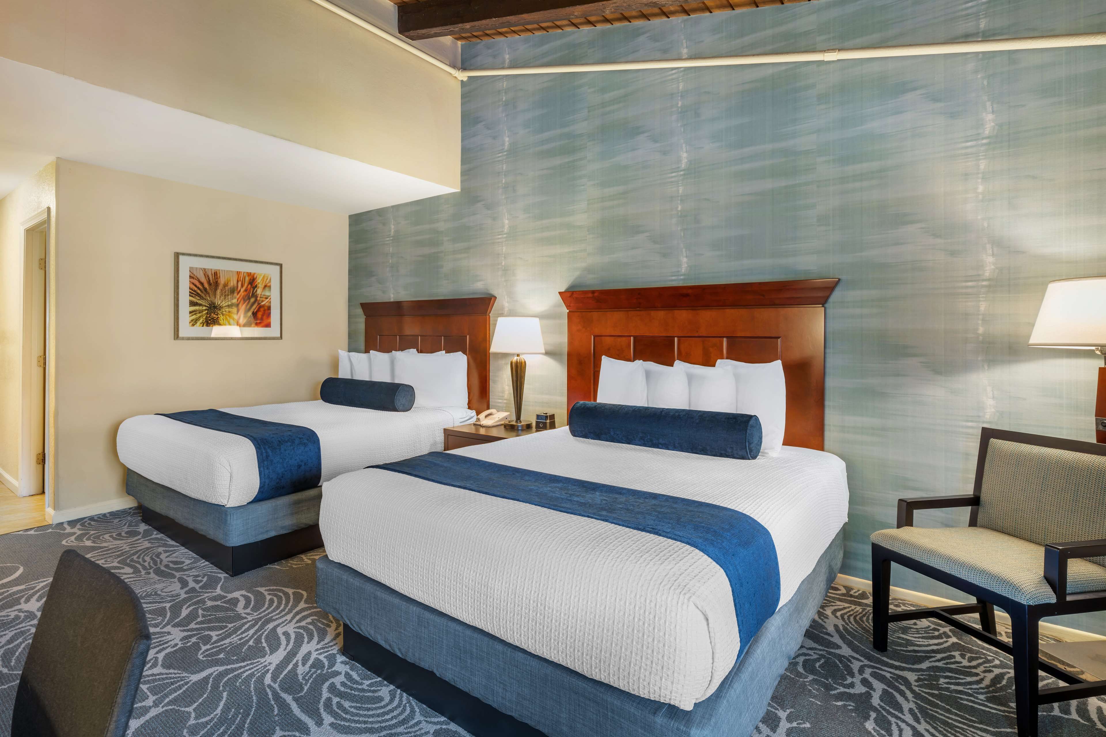 A hotel room with two beds, a chair, and a painting on the wall.
