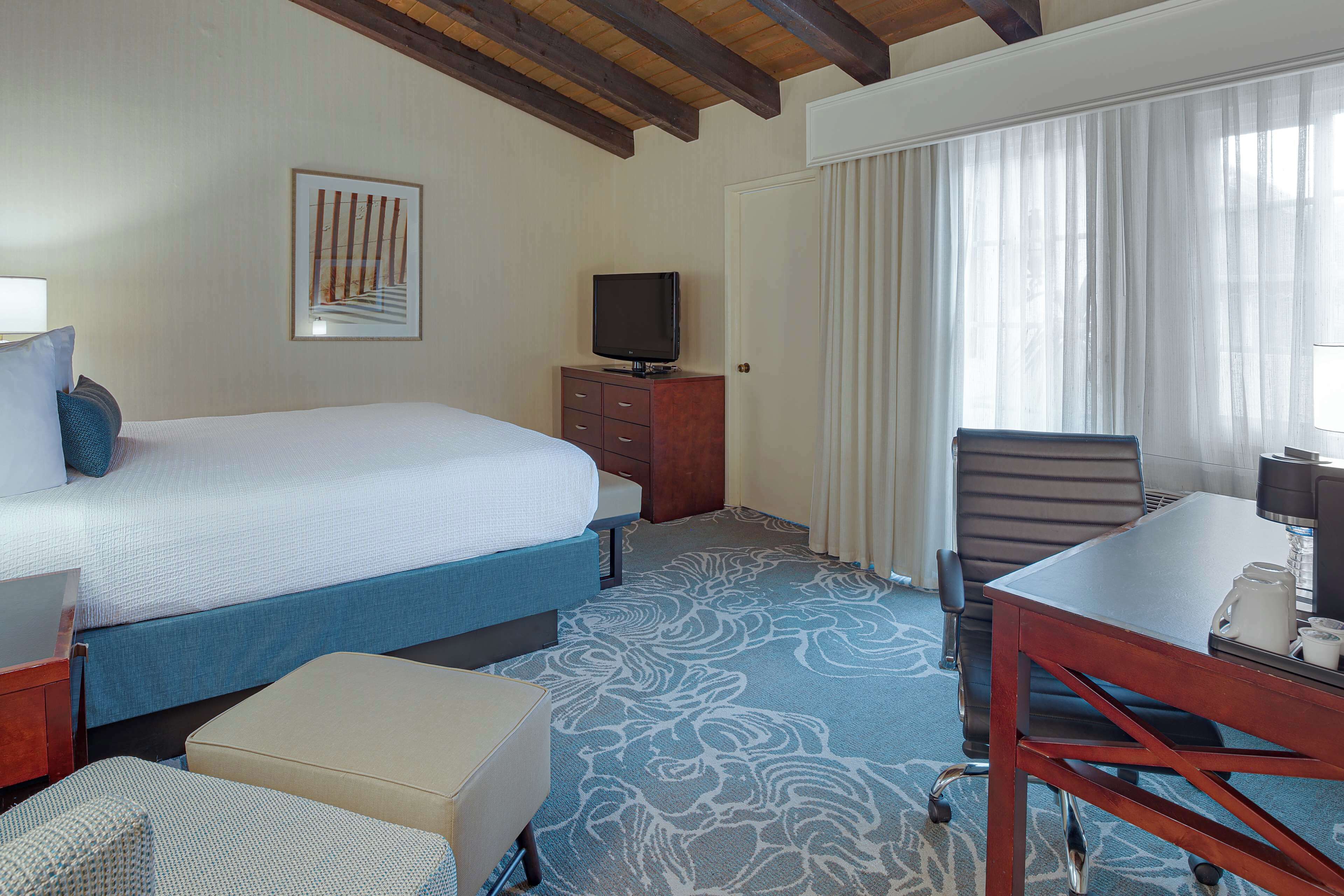 Une chambre d’hôtel équipée d’un lit, d’un bureau, d’une chaise, d’une télévision et d’une fenêtre avec des rideaux.