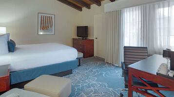 Une chambre d’hôtel équipée d’un lit, d’un bureau, d’une chaise, d’une télévision et d’une fenêtre avec des rideaux.
