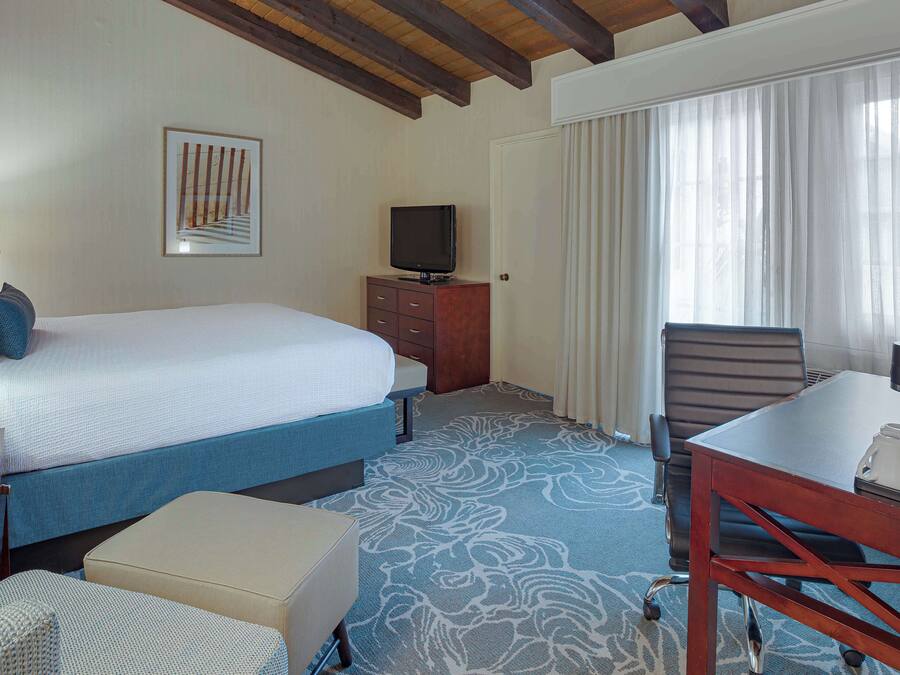 Une chambre d’hôtel équipée d’un lit, d’un bureau, d’une chaise, d’une télévision et d’une fenêtre avec des rideaux.