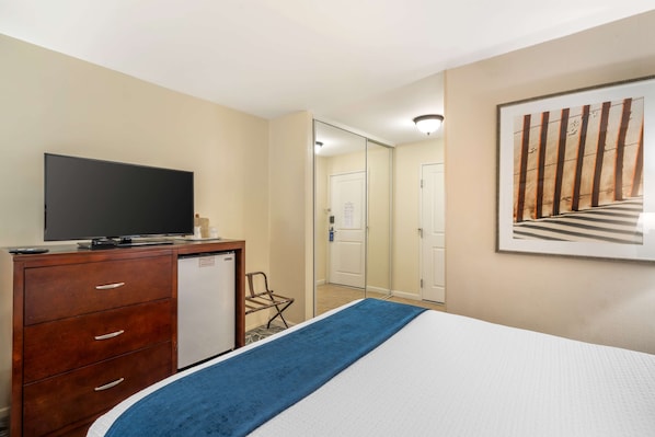 Habitació d'hotel amb un llit, una televisió sobre una cómoda de fusta, un refrigerador petit i una porta que condueix a una altra habitació.