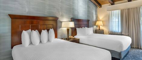 A hotel room with two beds, wooden headboards, and a large window with curtains.
