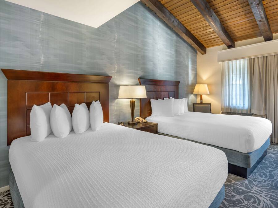 A hotel room with two beds, wooden headboards, and a large window with curtains.