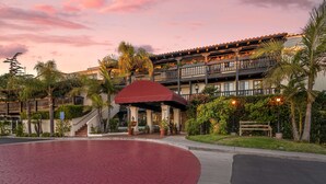 Un hotel con un patio de ladrillo rojo, varios balcones con plantas y una zona de entrada cubierta.