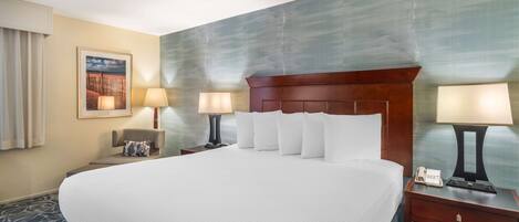 A hotel room with a large bed, two bedside tables with lamps, a nightstand, a framed picture on the wall, and a carpeted floor.