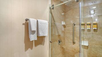Une salle de bain moderne avec une douche à parois de verre, un porte-serviettes avec deux serviettes et un distributeur de savon fixé au mur.