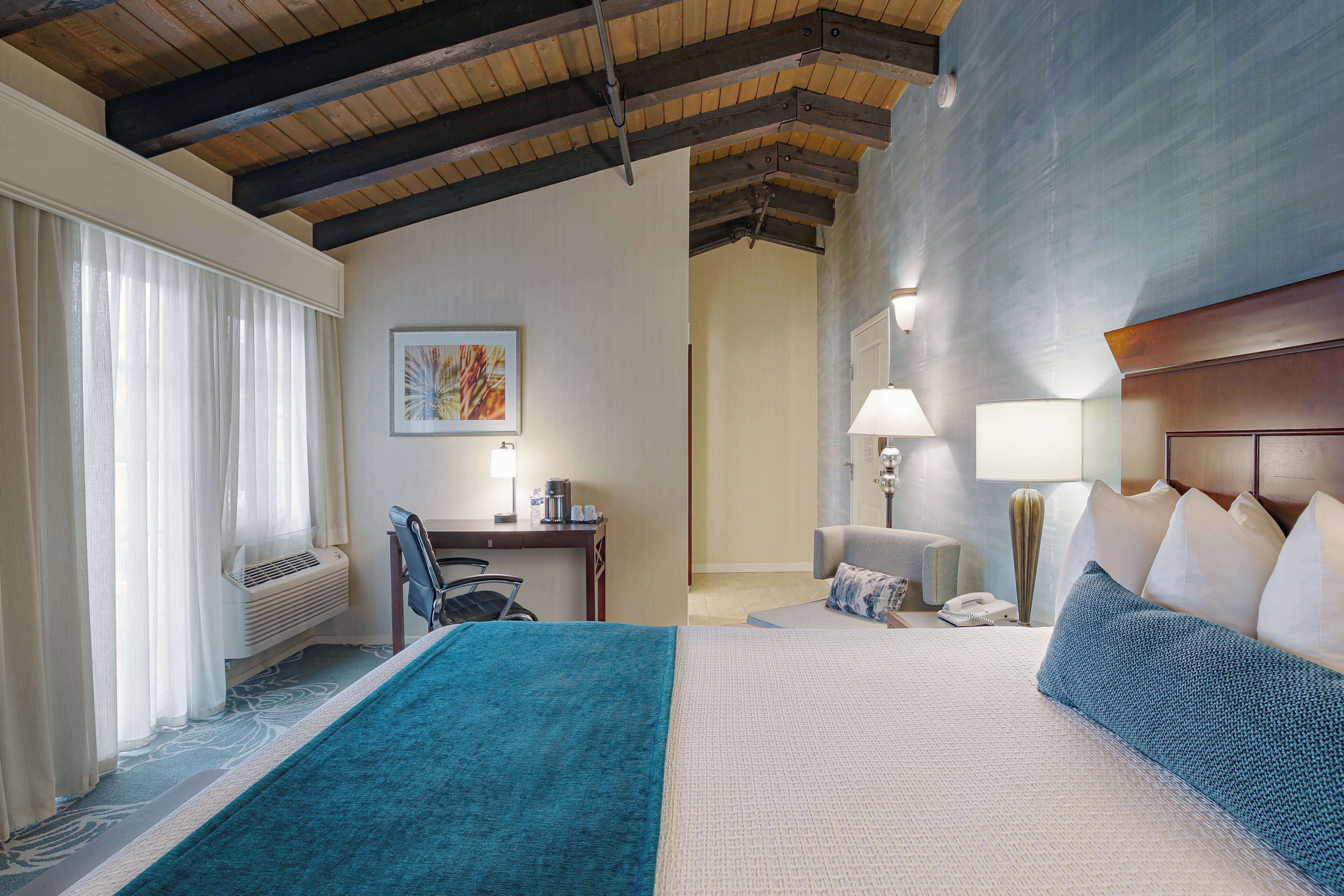A hotel room with a large bed, a desk with a chair, a lamp, and a painting on the wall.