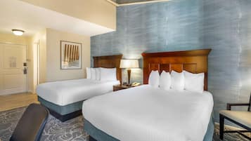 A hotel room with two beds, a desk, a chair, a lamp, and a framed picture on the wall.