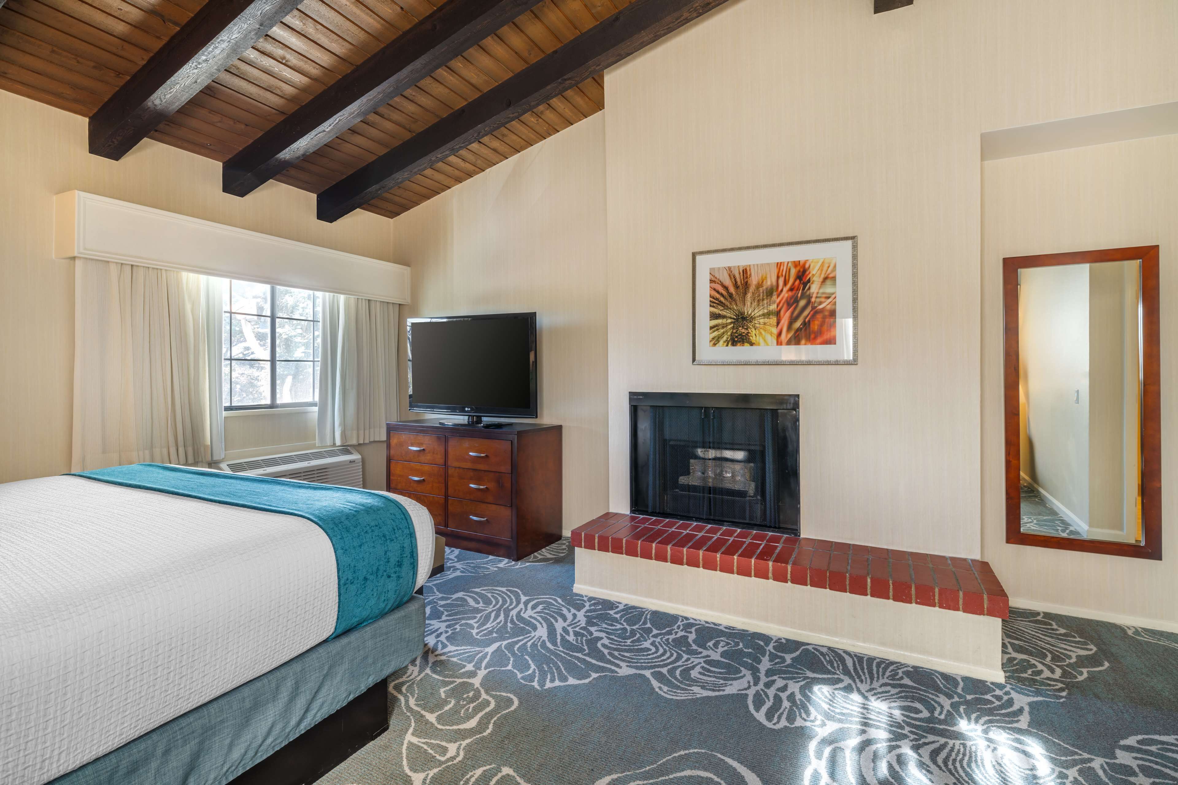 A hotel room with a bed, a television, a fireplace, and a large mirror.