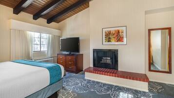 A hotel room with a bed, a television, a fireplace, and a large mirror.