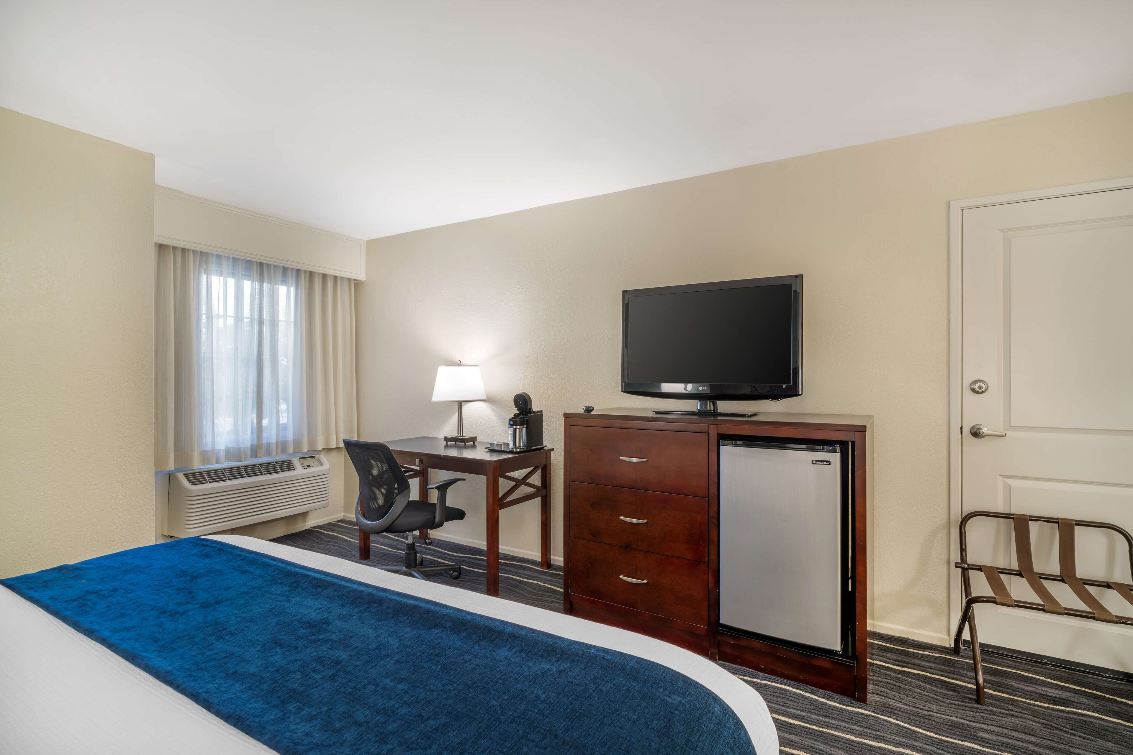 Ein Hotelzimmer mit einem Bett, einem Schreibtisch mit Computer, einem Fernseher, einem Stuhl und einer Tür.