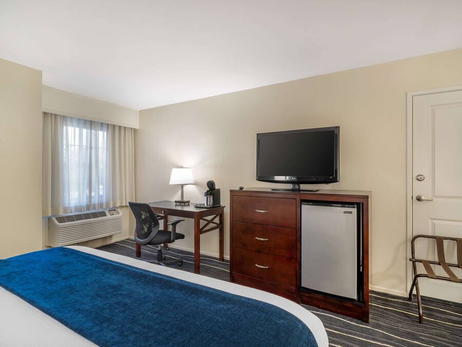 Habitación de hotel con cama, escritorio, computadora, televisor, silla y puerta.
