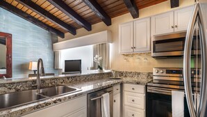 Una cocina moderna con encimeras de granito, electrodomésticos de acero inoxidable, armarios blancos y techo de madera.
