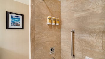 A shower with a handrail, a framed picture on the wall, and three bottles of shampoo.