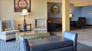 A hotel lobby with a seating area featuring a sofa, armchairs, and a leather chair. There is a lamp on a side table, a mirror on the wall, and a patterned rug on the floor. - Quality Inn Thief River Falls (Thief River Falls)