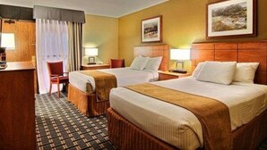 A hotel room with two beds, a desk, a chair, and a small table. There are two lamps on the nightstands and a painting on the wall. - Quality Inn Thief River Falls (Thief River Falls)