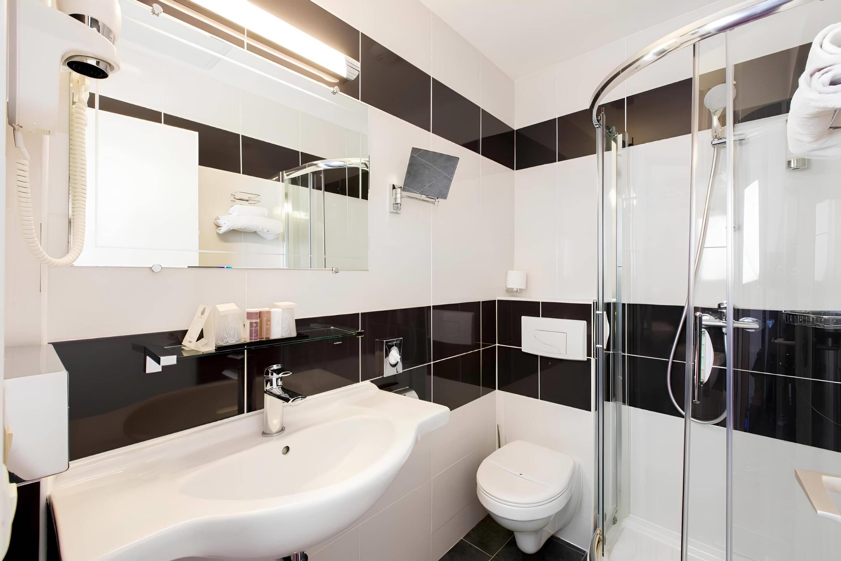 A modern bathroom with a white sink, a toilet, a glass shower enclosure, and a mirror with a towel rack.