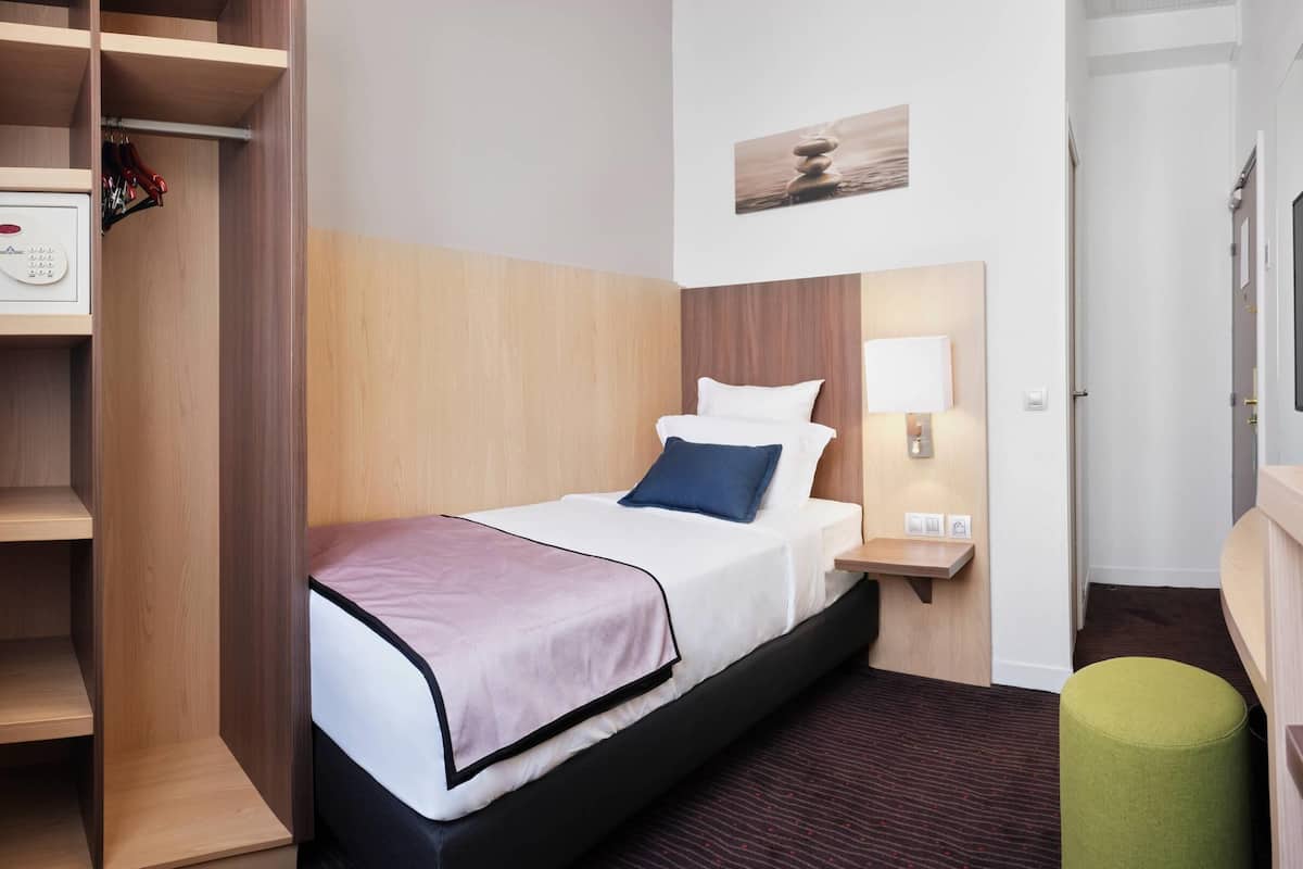 A hotel room with a bed, a wardrobe, a bedside table, a lamp, and a television.