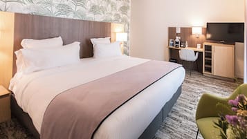 Una habitación de hotel con una cama grande, un escritorio con una silla, un televisor y un mueble bajo.