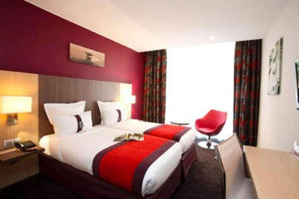 A hotel room with a large bed, two bedside tables, a desk, a chair, and a view of the outdoors.