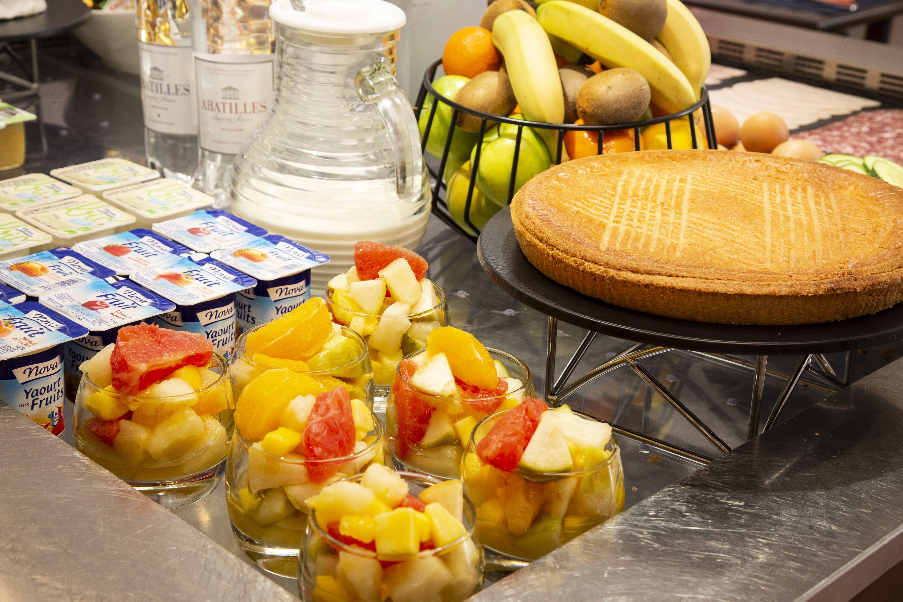 A breakfast buffet with various fruits, a pitcher of milk, and packaged yogurt.