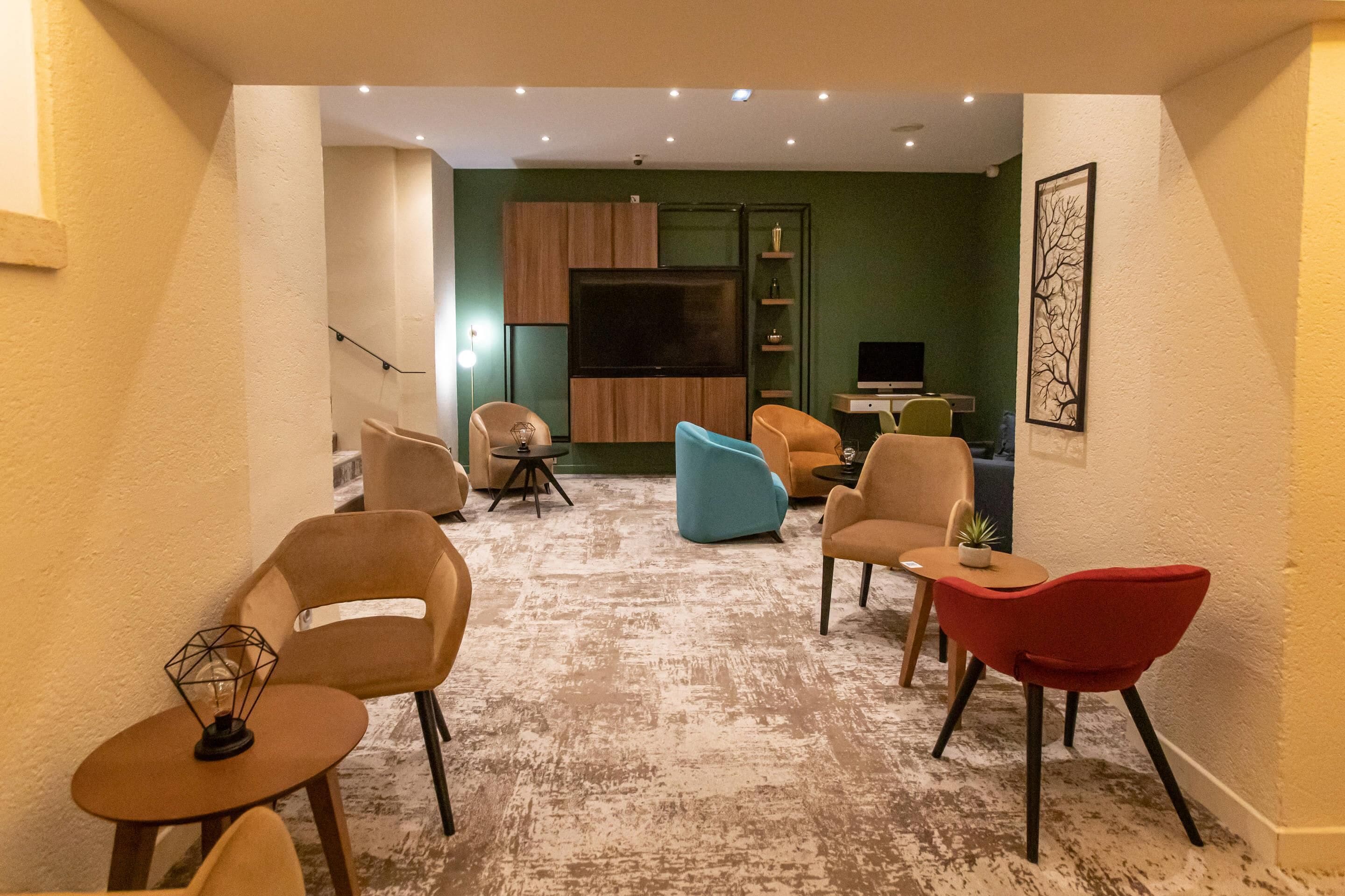 Un salon équipé d’un téléviseur à écran plat, de plusieurs fauteuils, d’une table basse et d’une petite table sur laquelle est posée une plante.