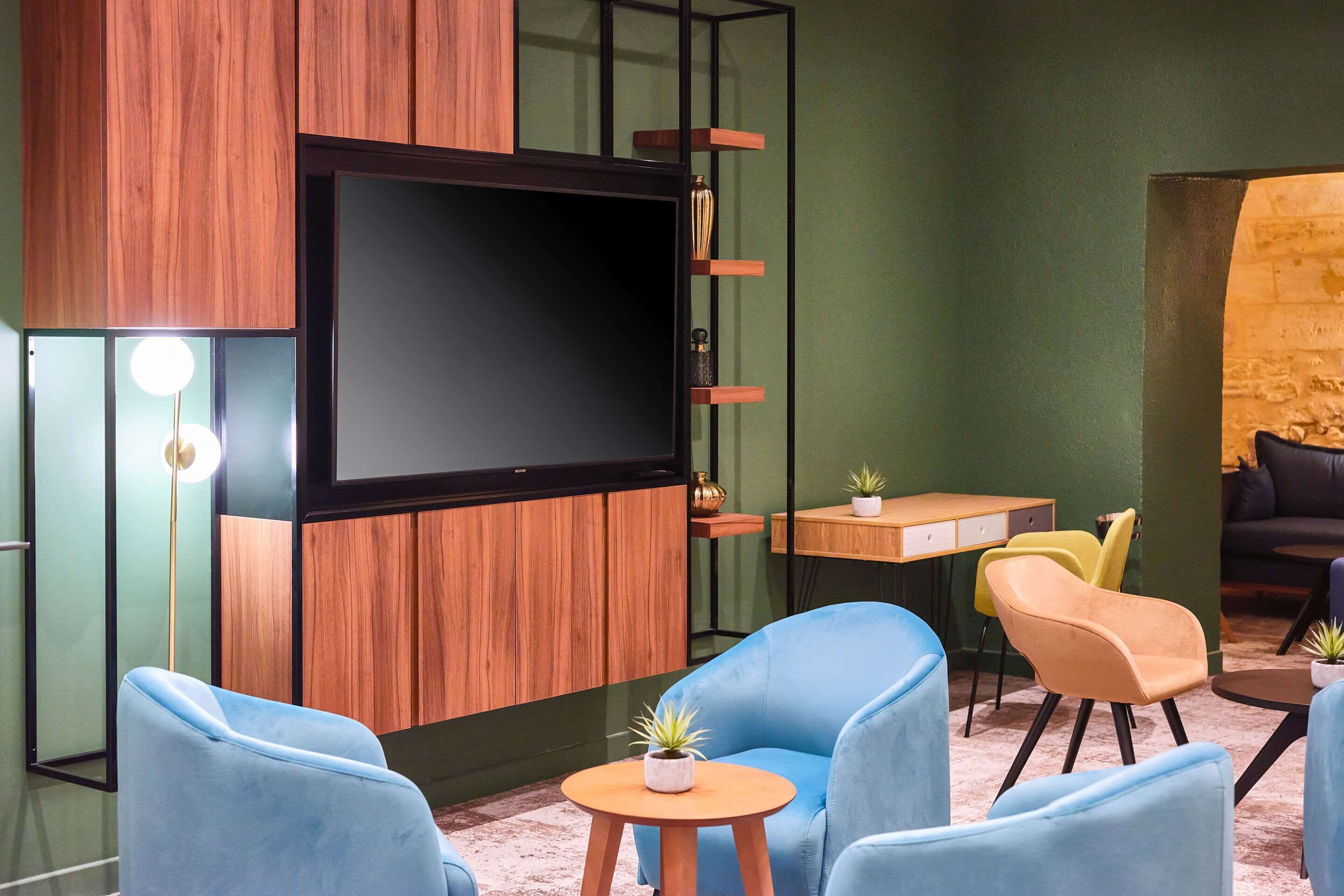 Una sala moderna con una televisión de pantalla plana montada en una pared de paneles de madera, una pequeña mesa de madera y dos sillones azules.