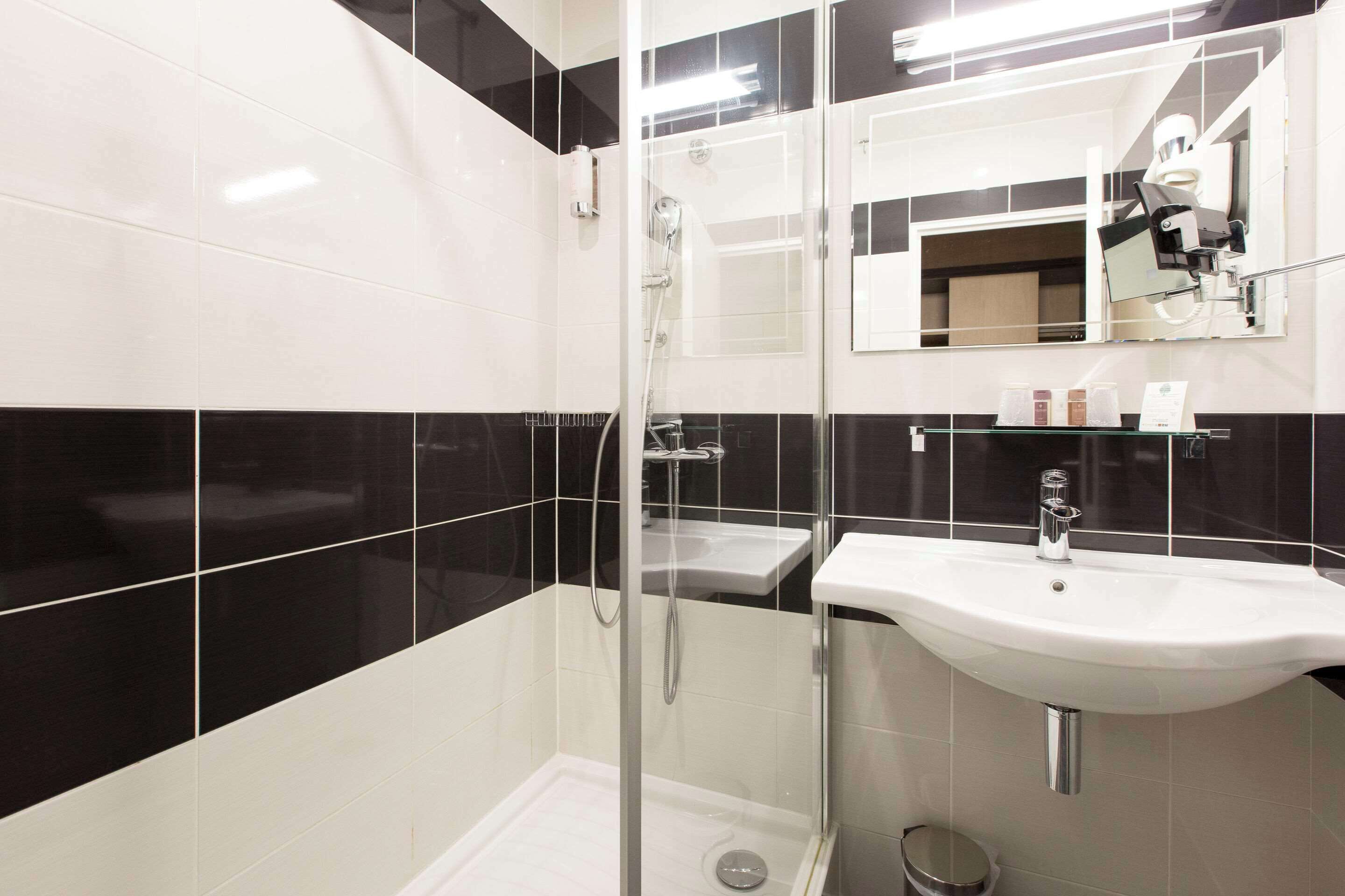 Un baño moderno con ducha acristalada, lavamanos blanco y espejo sobre el lavamanos.