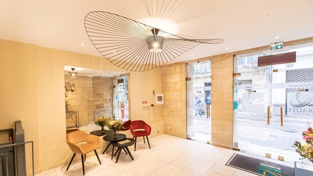 A reception area with a modern ceiling design, a glass door entrance, and a seating arrangement with a table and chairs.