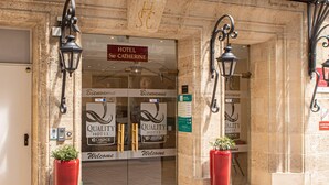A hotel entrance with a sign reading 'HOTEL Ste CATHERINE,' two red planters, and 'QUALITY HOTEL' branding.