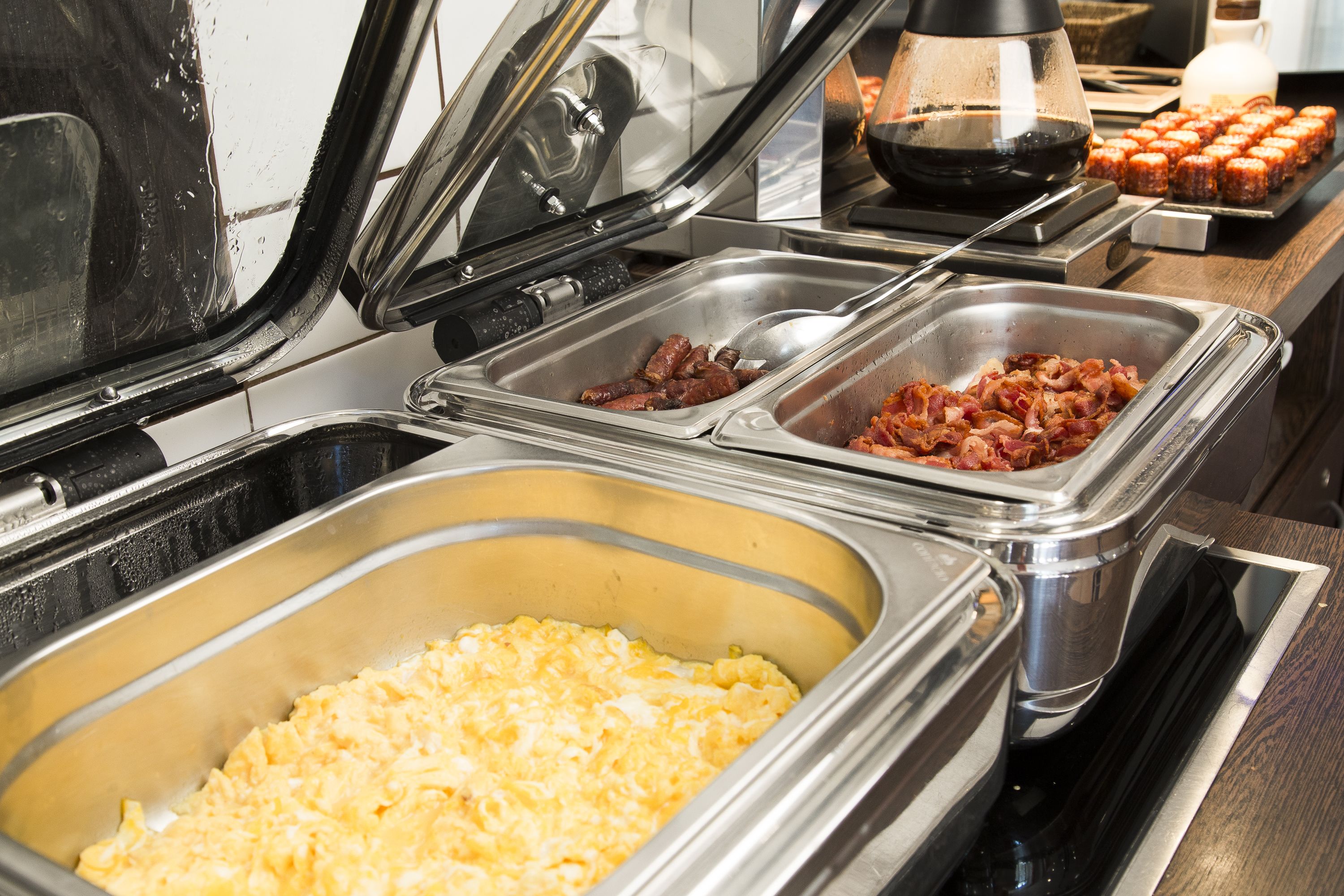 A buffet with various food options including scrambled eggs, bacon, and sausages.