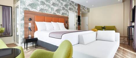 A hotel room with a bed, green armchairs, a white sofa, a small table, and a wall with a leaf pattern.