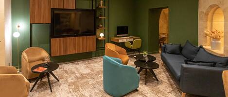 Una sala de estar moderna con una televisión de pantalla plana, un escritorio con computadora y asientos cómodos, incluyendo un sofá y sillones.