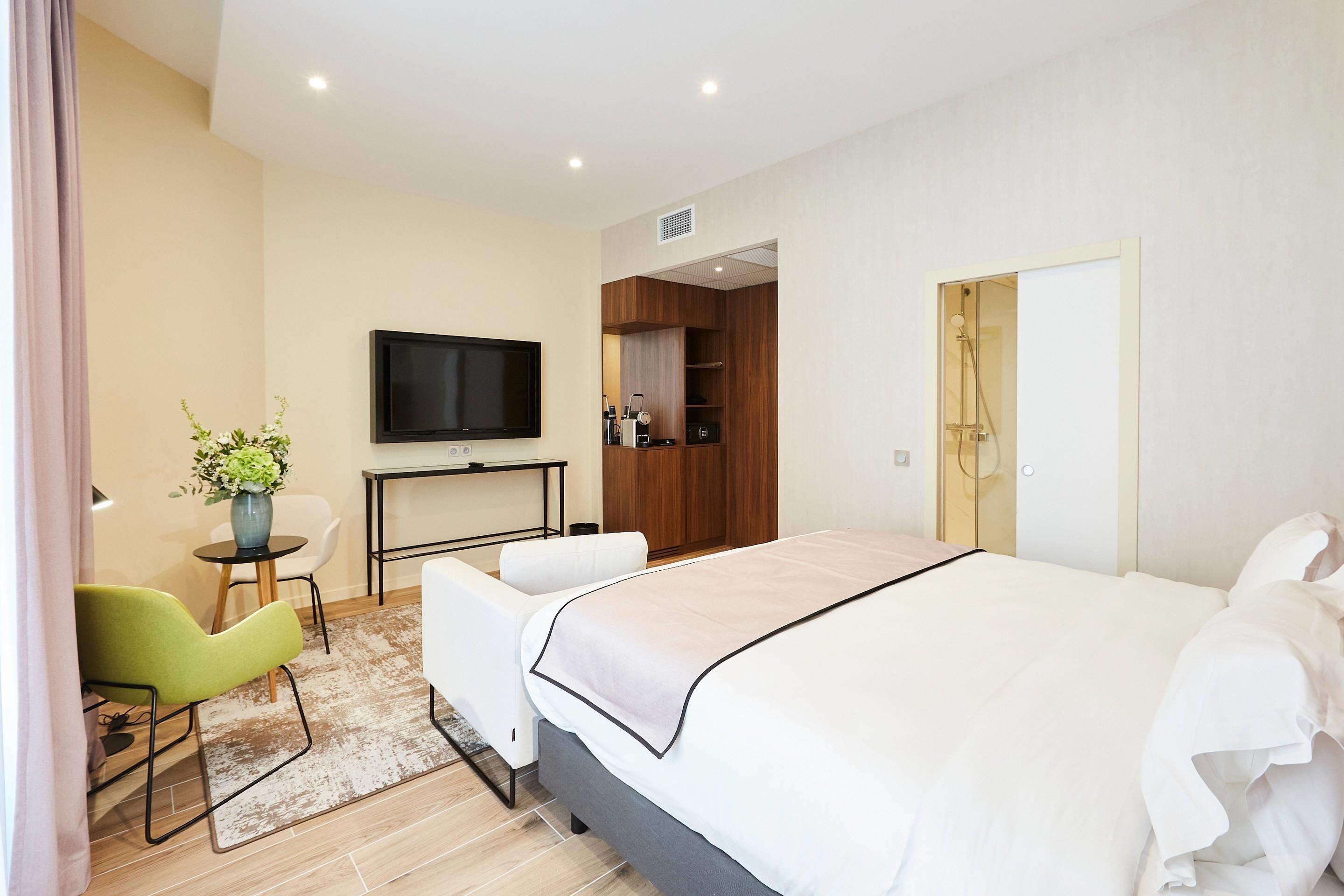 A modern hotel room with a bed, a television, a desk, and a seating area.