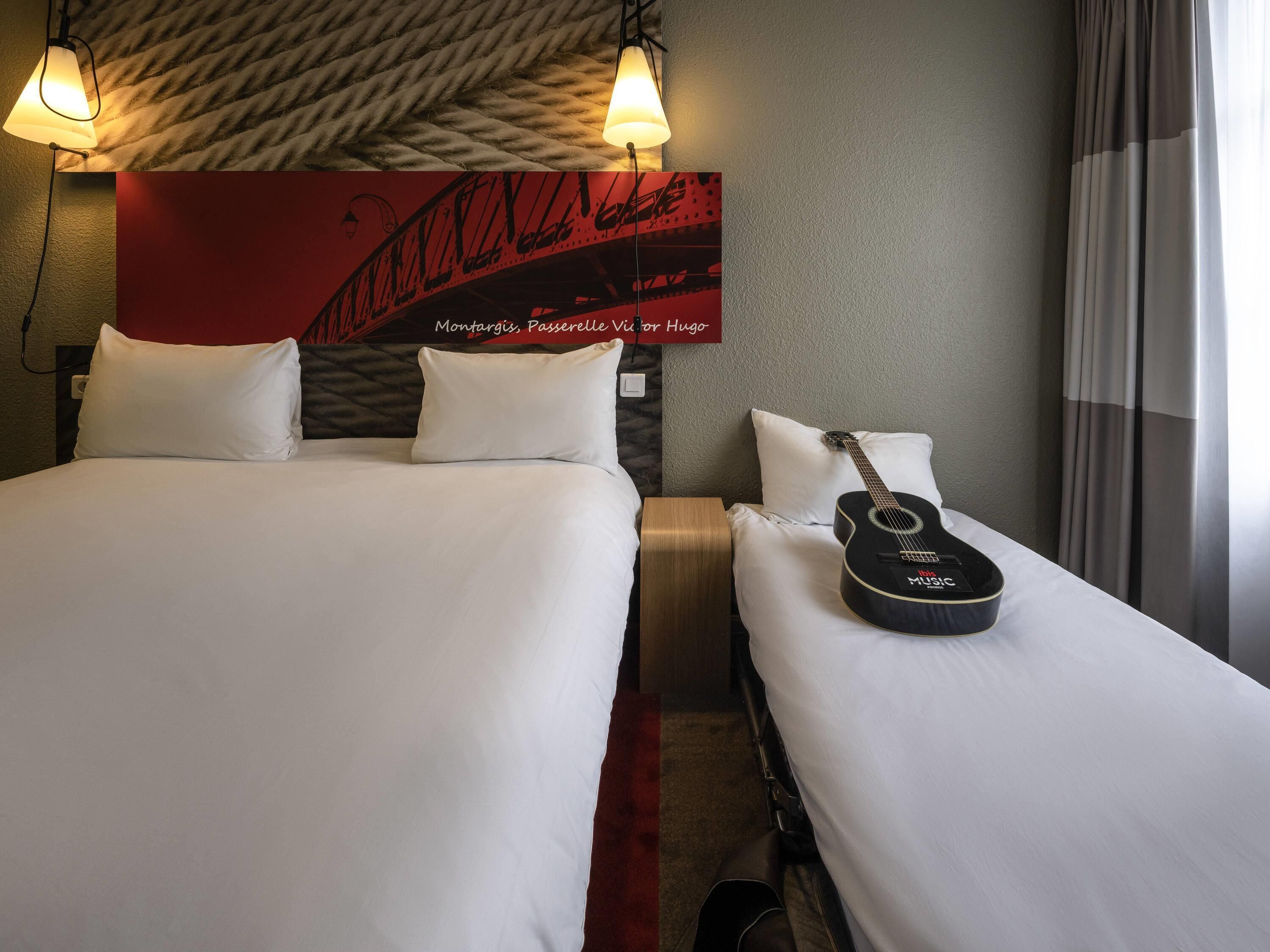 Habitación de hotel con dos camas, una guitarra y una pared roja decorada con notas musicales.