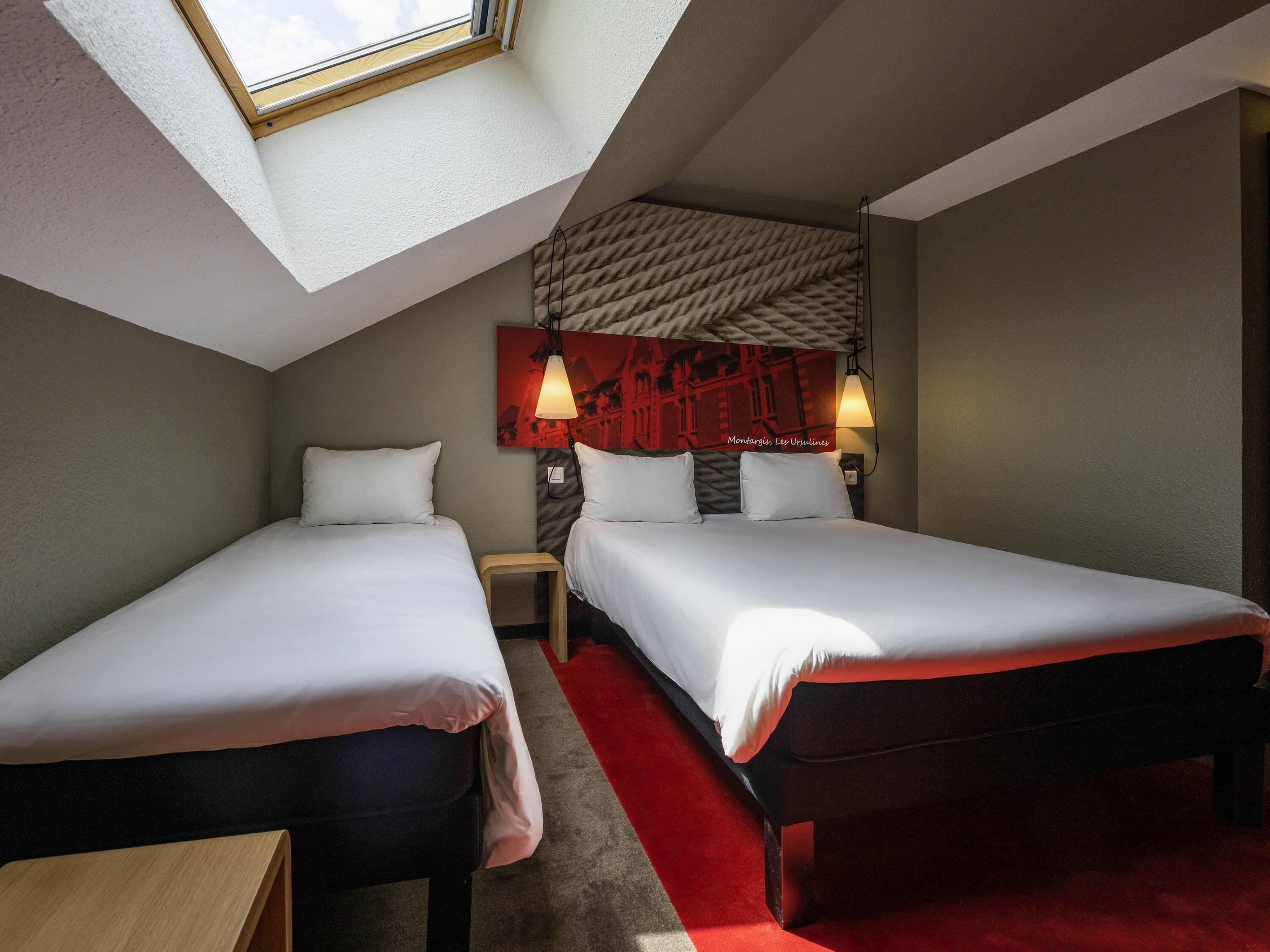A hotel room with two beds, a skylight, a red carpet, and a wall-mounted lamp.