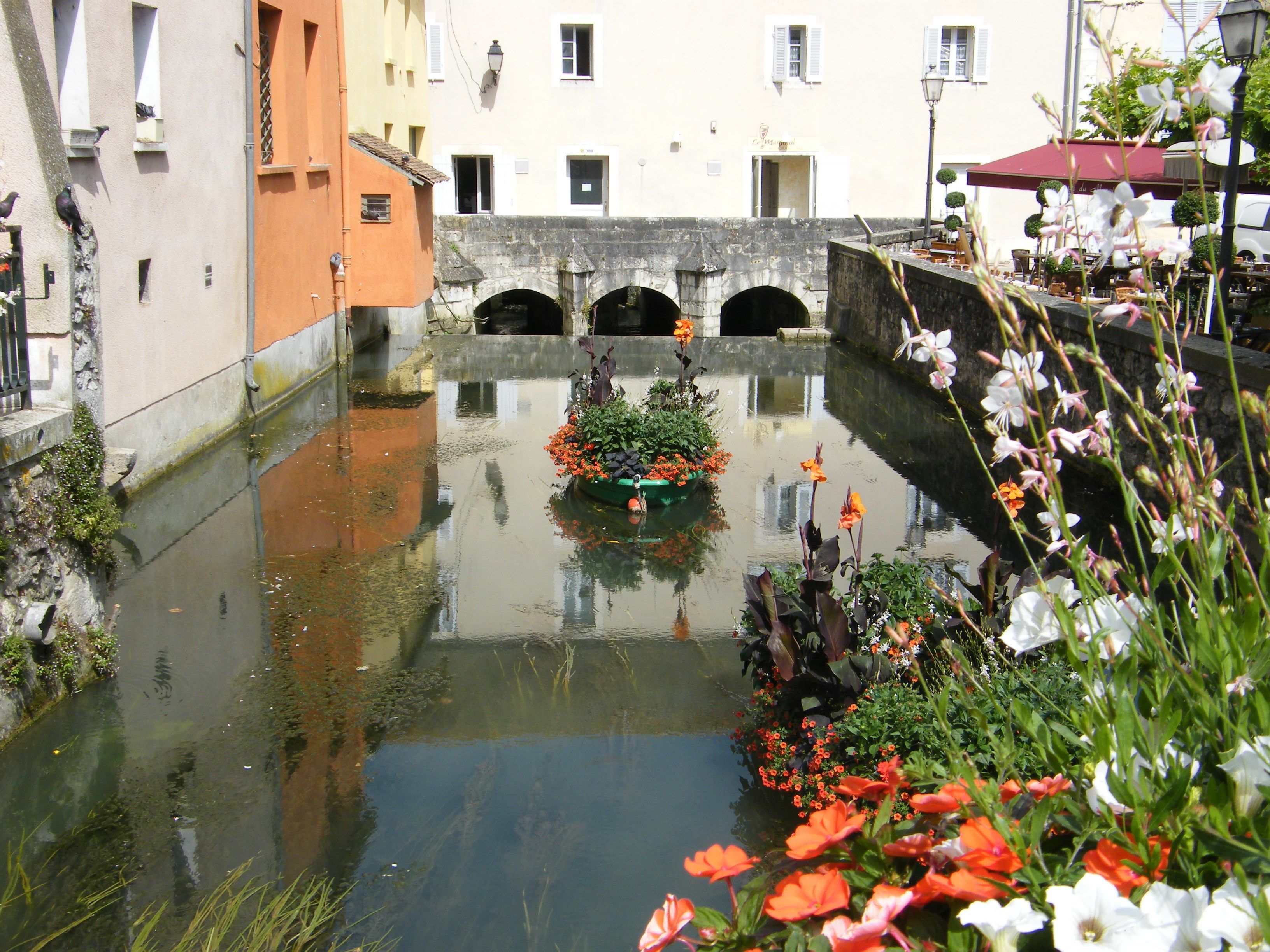 A canal with a bridge, buildings, and a flower bed.