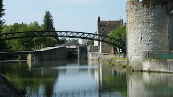 A stone bridge over a calm river, a castle-like building, and a clear sky.