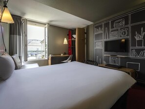 Habitación de hotel con una cama grande, un escritorio, una silla, un televisor y una ventana con cortinas.